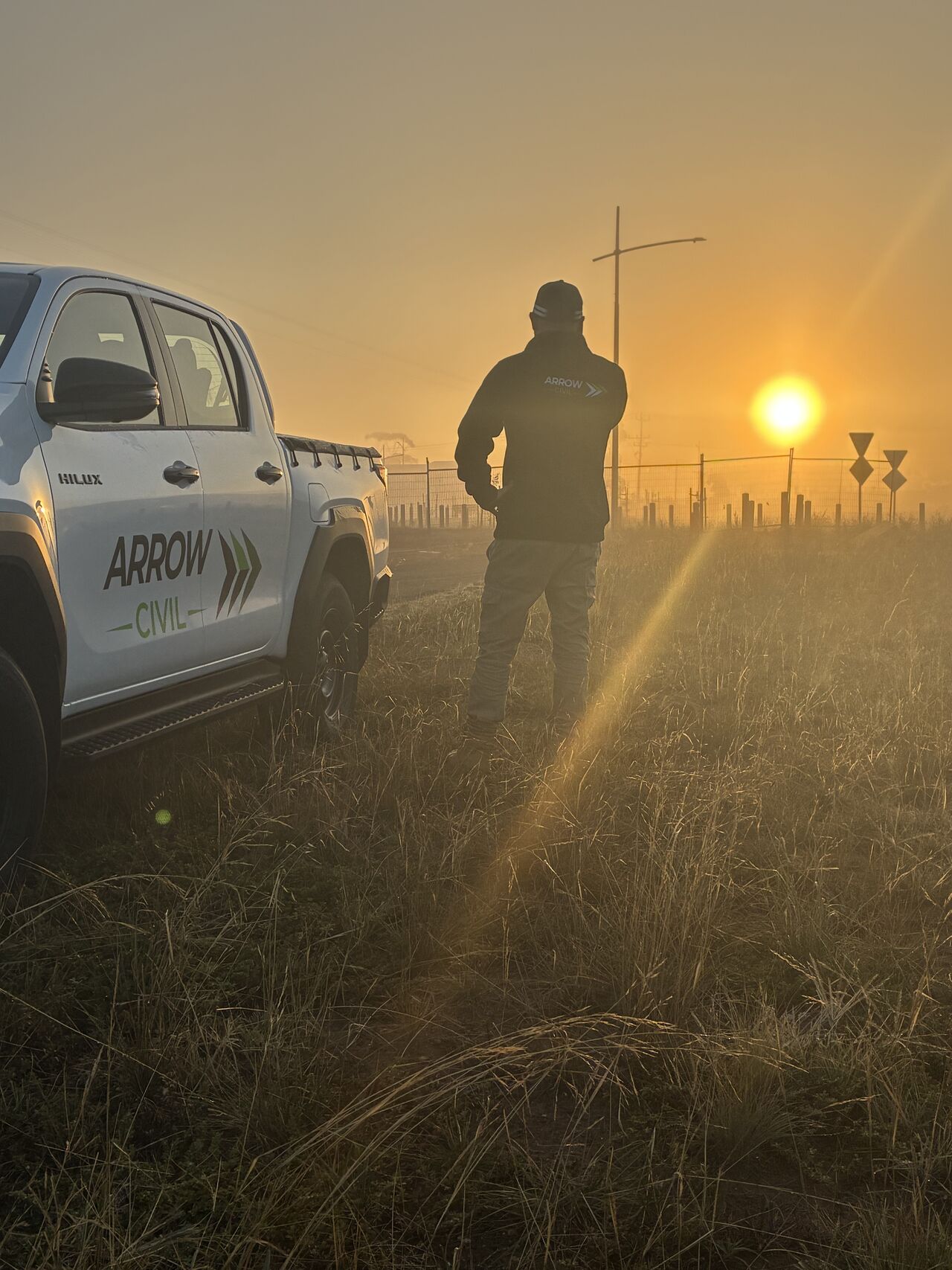 An Arrow Civil team member on site at sunrise beside a branded Arrow Civil ute