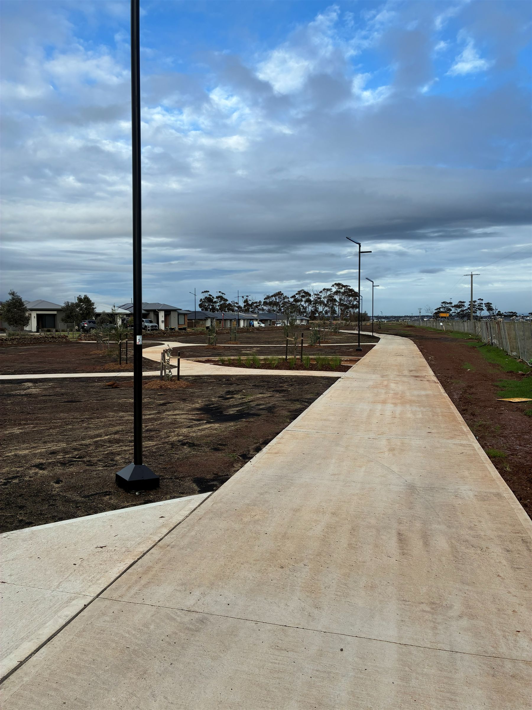 Freshly poured concrete shared path and topsoiled earthworks through a residential subdivision